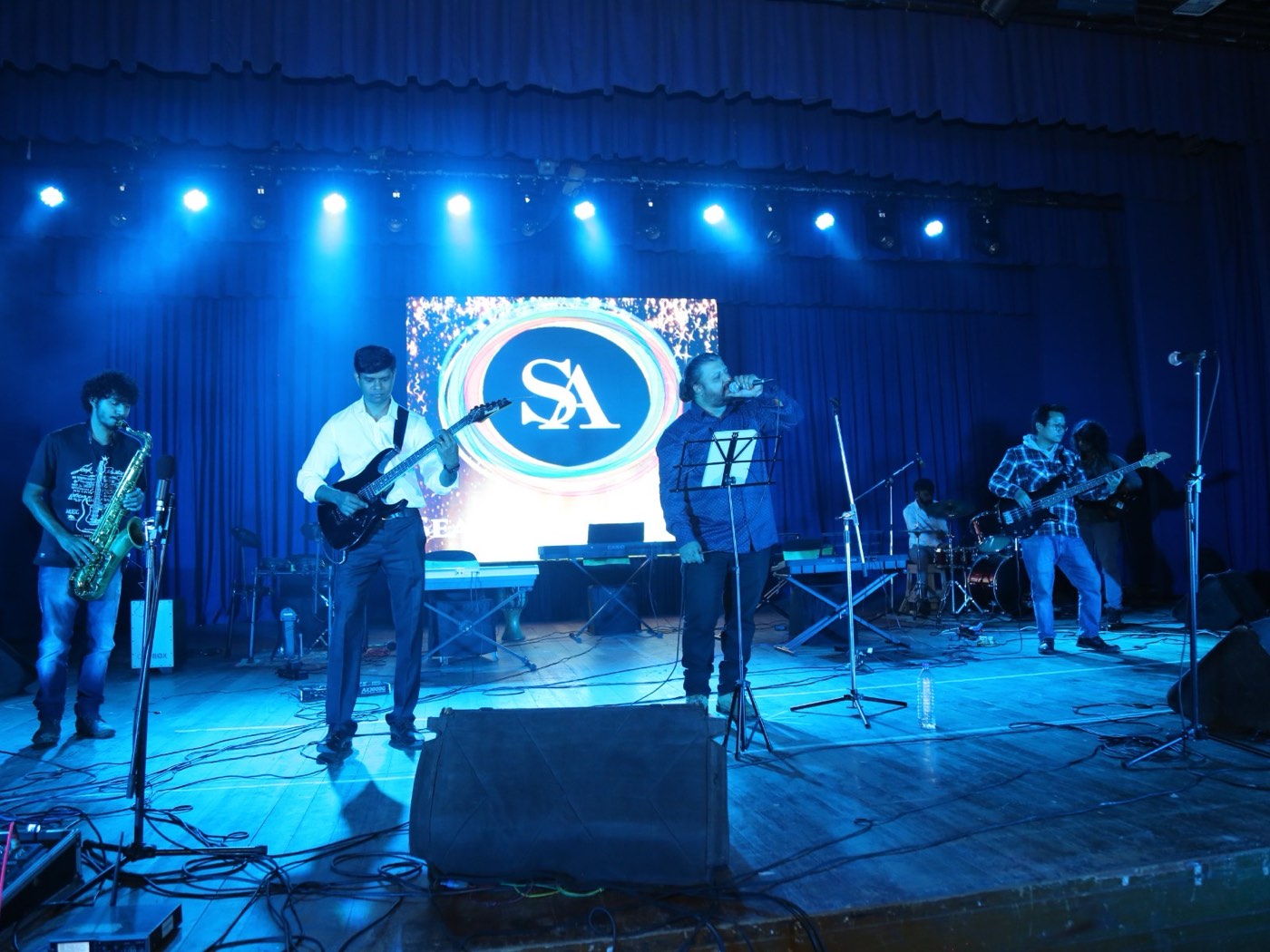 Live band performing in front of the LED wall showing the Seasons Music Academy logo
